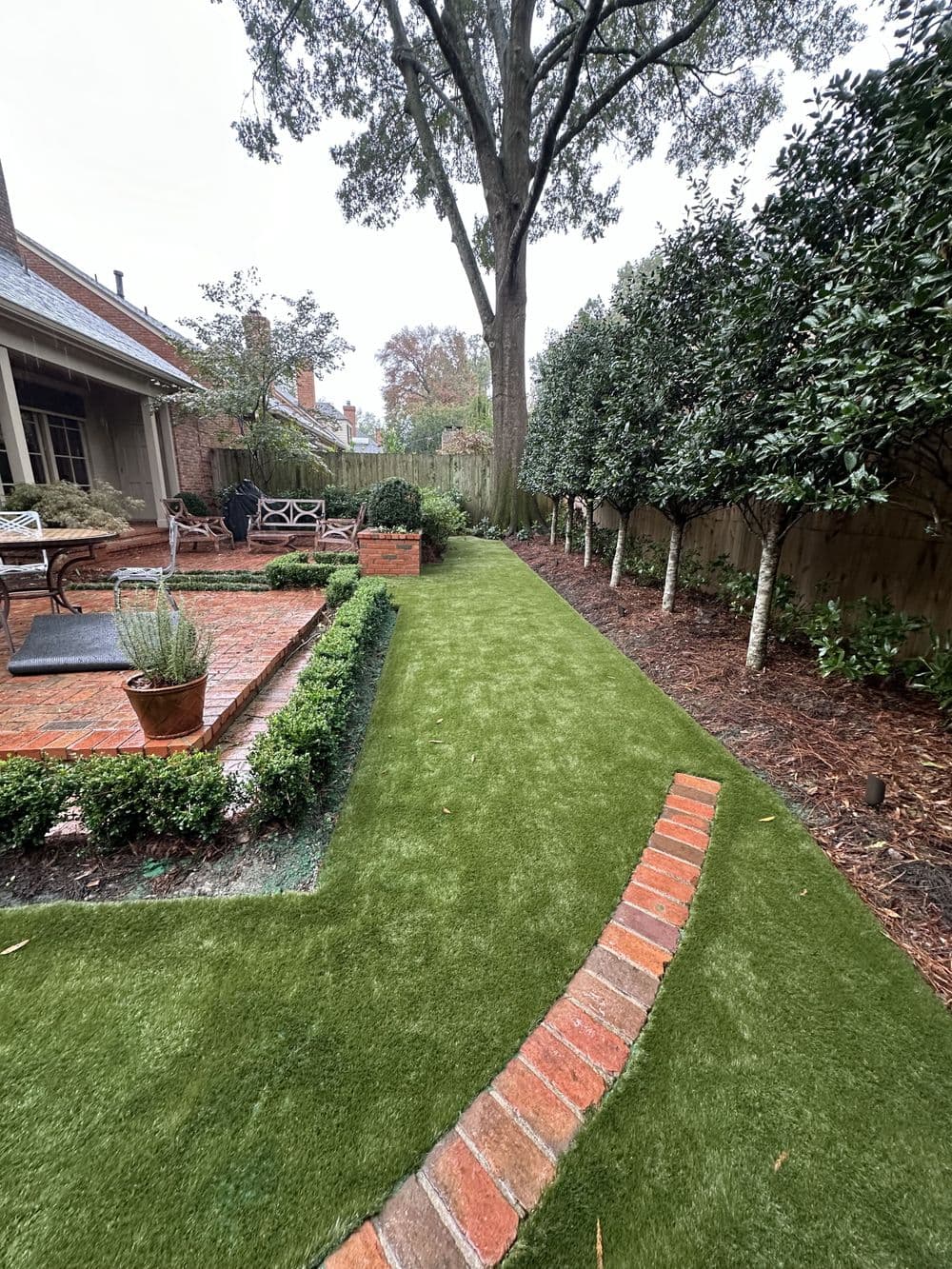 Lush green artificial lawn with brick pathway and landscaped border in a serene backyard.