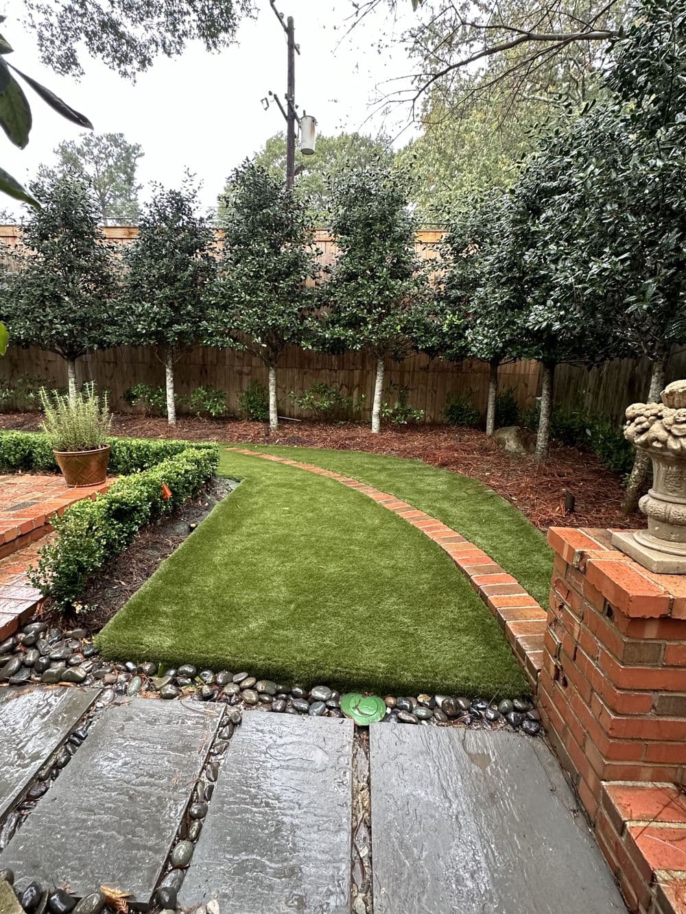 Lush green lawn with curved path, surrounded by trees and brick landscaping in a serene garden.